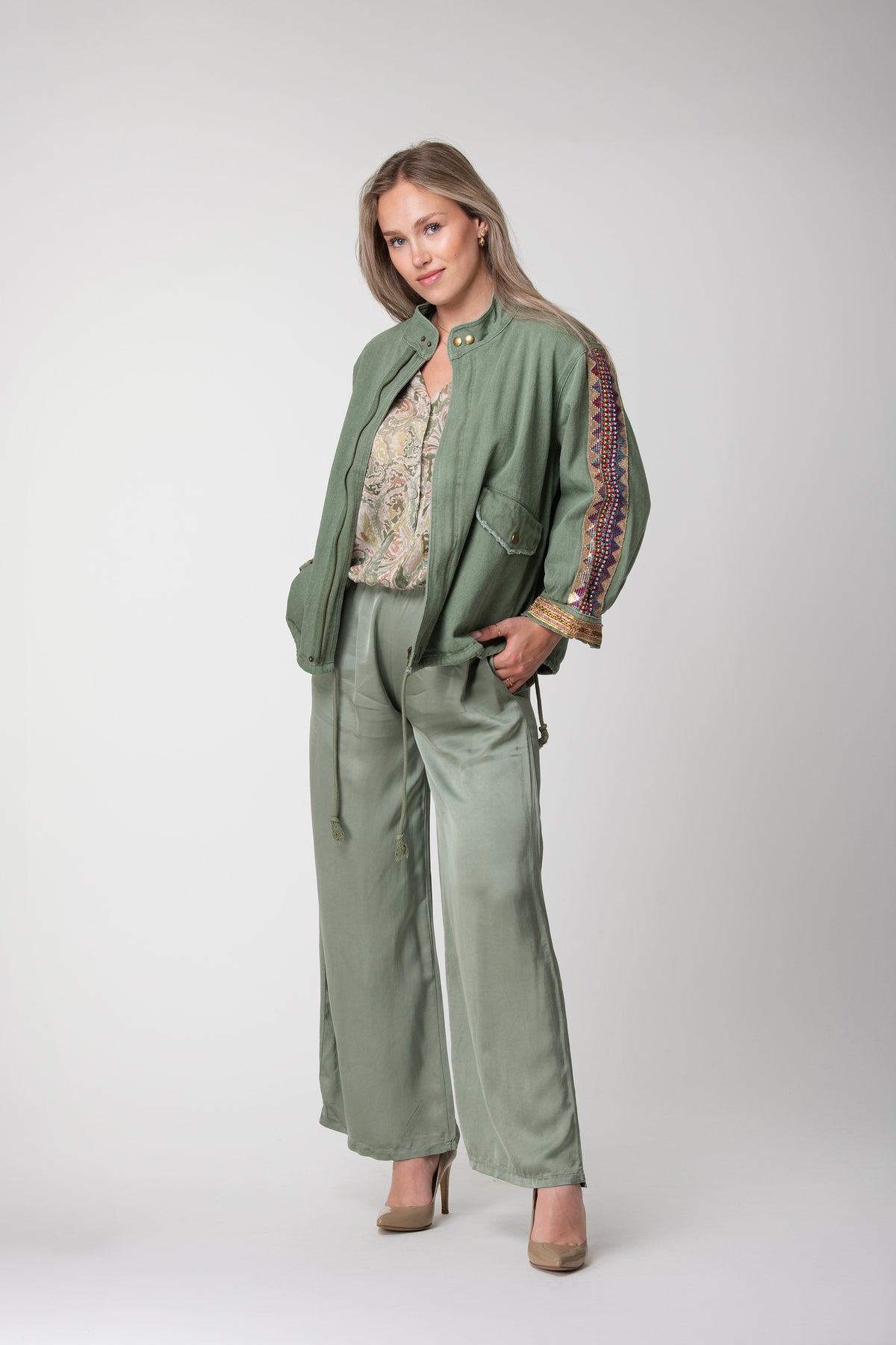 Model wearing a sage green jacket with colourful embroidered sleeve panels