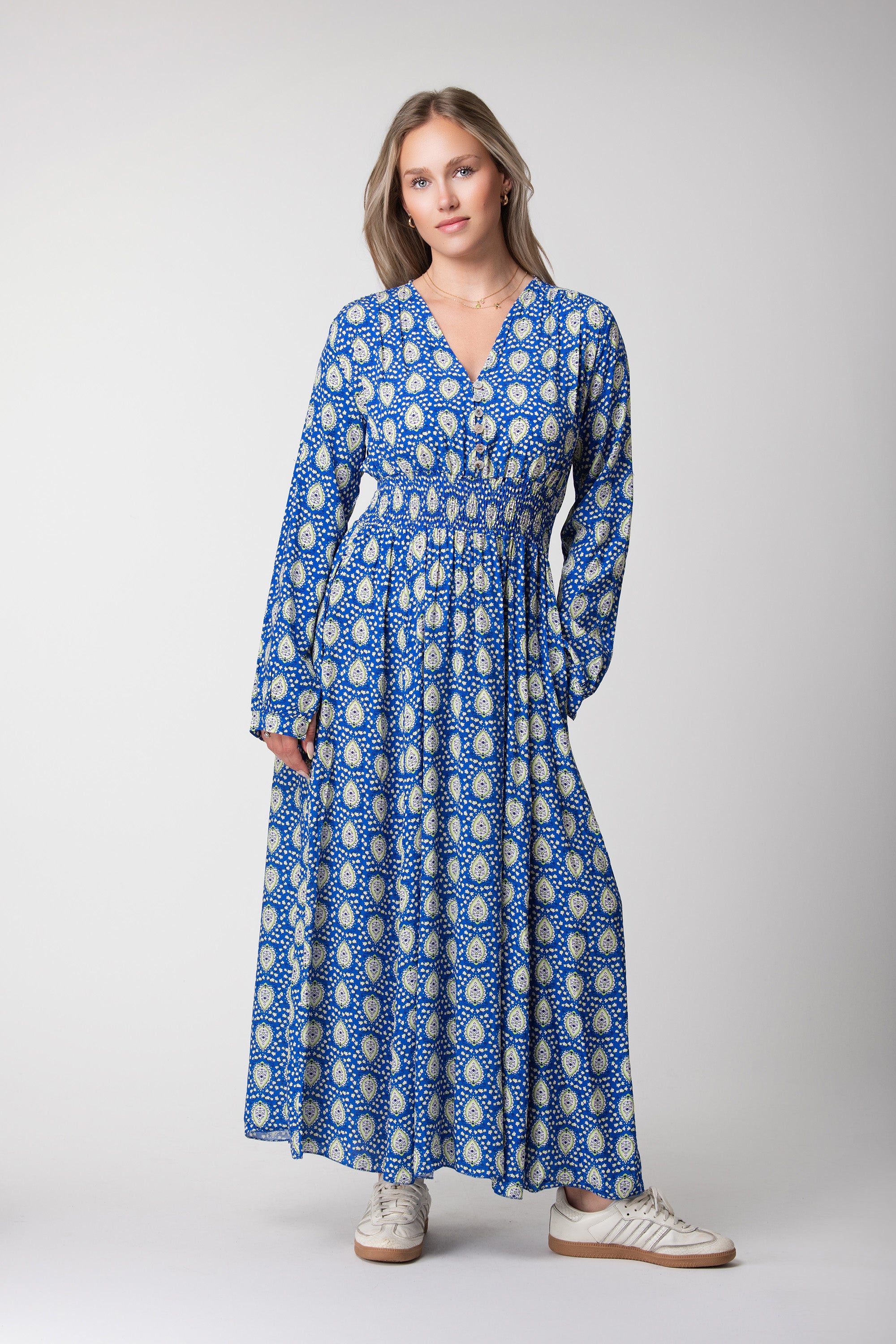 Model wearing a blue maxi dress with green and cream motifs, long sleeves and a V-neckline