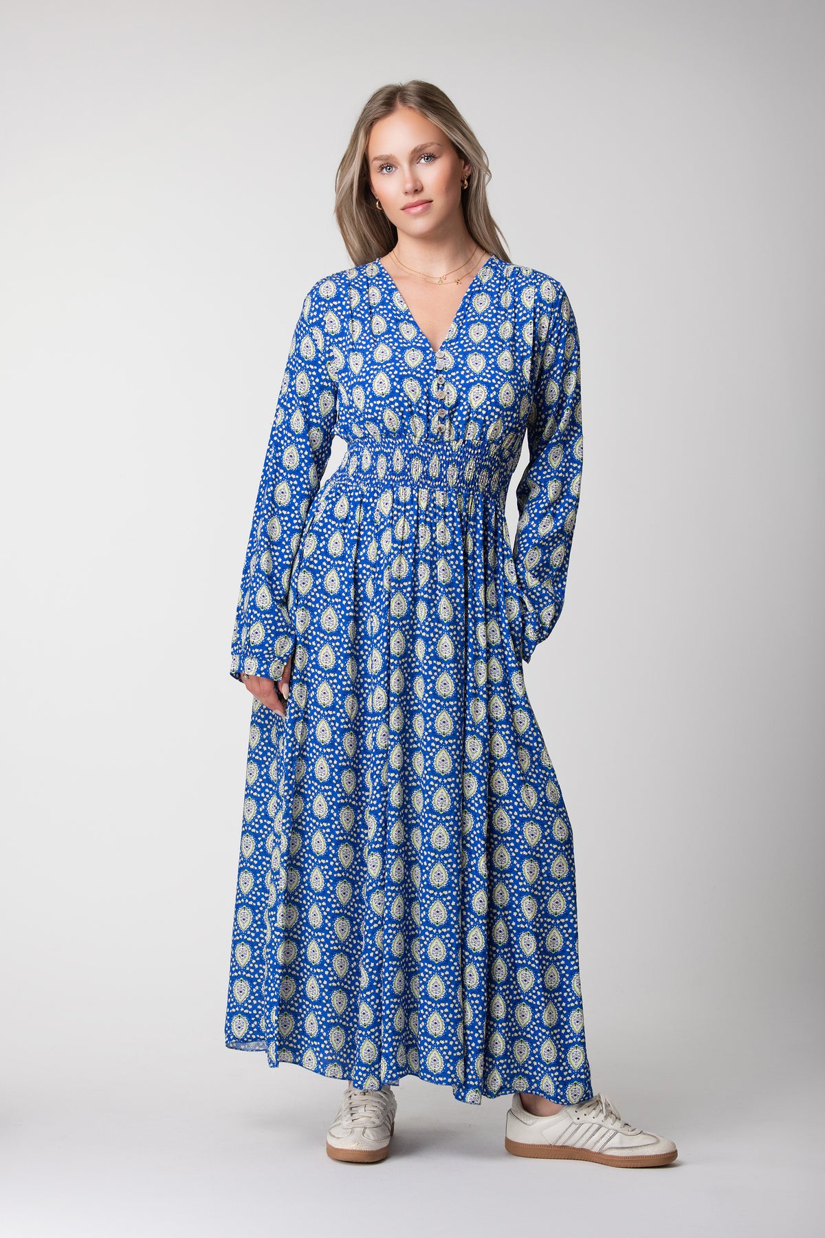 Model wearing a blue maxi dress with green and cream motifs, long sleeves and a V-neckline